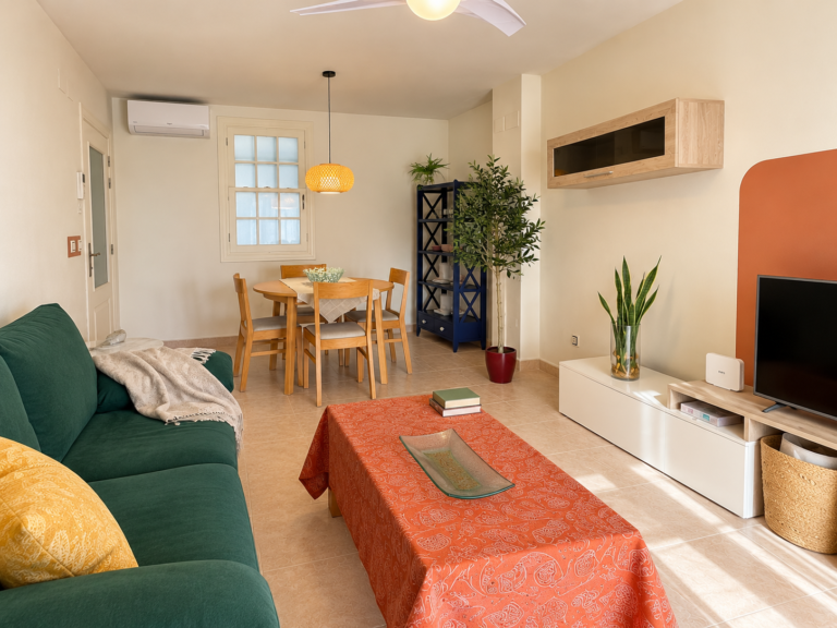 Vista del salón comedor de Ático MarLuc con sofá verde, televisión y mesa de comedor